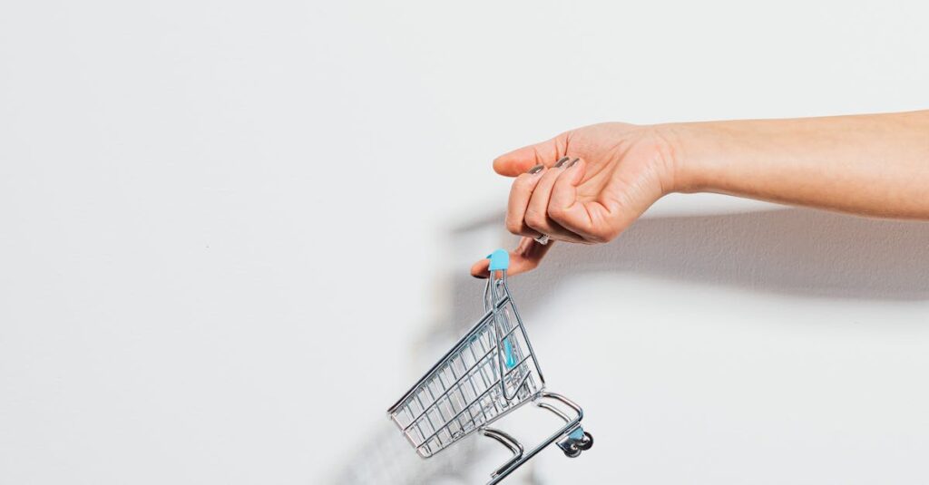 A hand holding a miniature shopping cart against a clean white background, emphasizing simplicity.